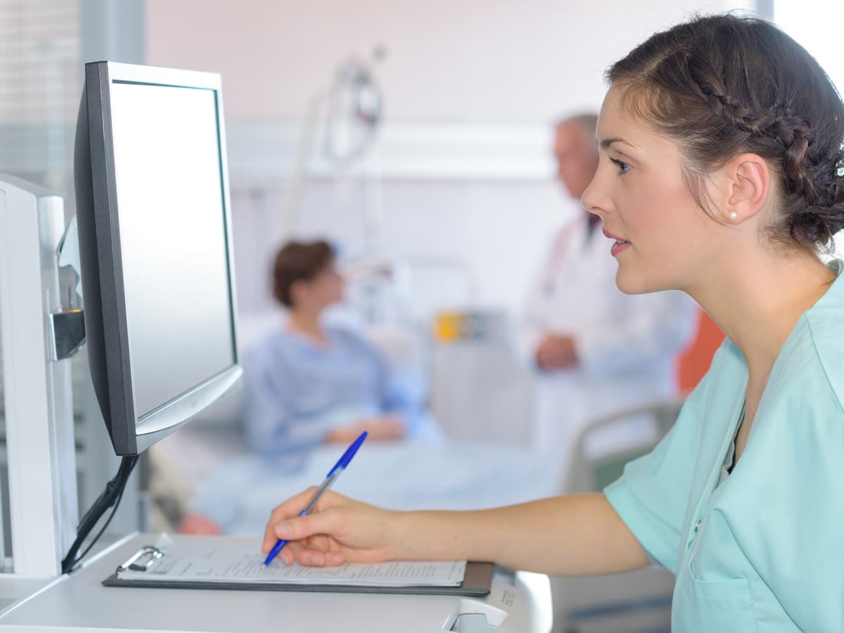 Medical assistant filling out paperwork on a computer.