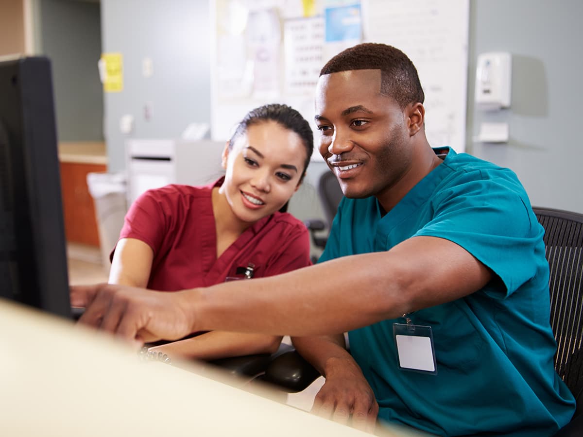 Physician and billing specialist pointing at a monitor and smiling.