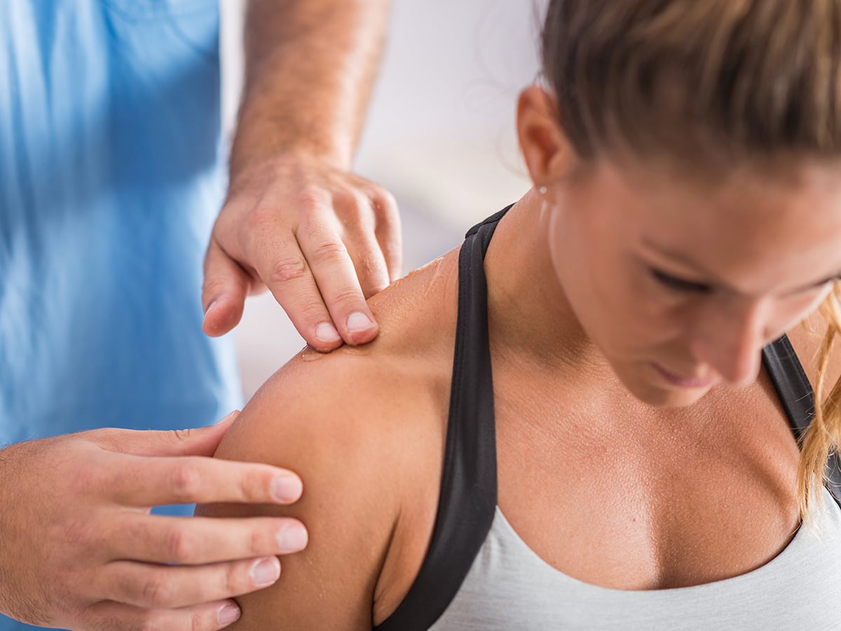 Massage therapist examining an athlete's shoulder.